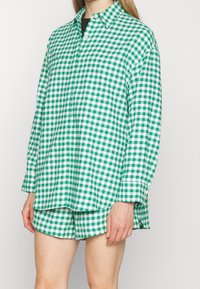Green and white checked shirt made of fabric, featuring a collar, long sleeves, and a relaxed fit, paired with matching shorts.