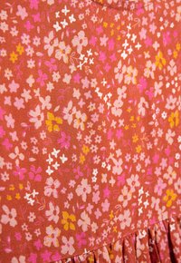 Stoff mit Floral-Muster, der pinke, gelbe und weiße Blumen auf einem rostfarbenen Hintergrund zeigt; strukturiert mit einem rüschierten Saum am unteren Ende.