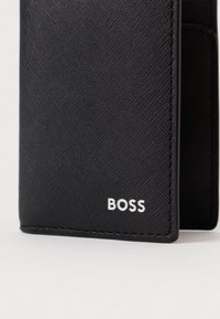 Μαύρο πορτοφόλι από υλικό με υφή, με ορατό το όνομα της μάρκας "BOSS" σε λευκό χρώμα. Ο σχεδιασμός είναι λιτός με καθαρές άκρες.