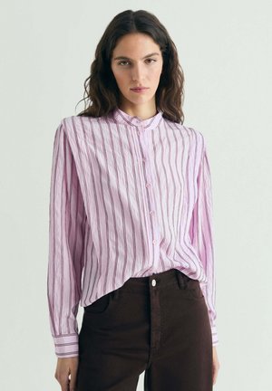 Mujer de pie vistiendo una camisa de botones de rayas rosas, pantalones anchos de pierna oscura con puños y sandalias negras de plataforma con punta abierta.