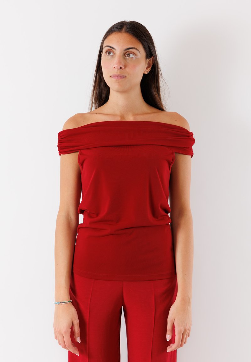 Top rosso scollato con dettagli di tessuto arricciato, texture morbida, design aderente, abbinato a pantaloni rossi coordinati per un look coerente.
