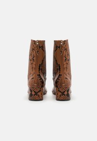 Botas de tobillo de piel sintética en color marrón con un patrón de serpiente, con una textura suave, un tacón ancho y cremalleras laterales. Presentan escamas distintivas y un diseño elegante.