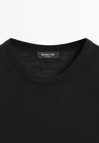 Maglione nero a girocollo con etichetta del marchio "Massimo Dutti" visibile cucita all'interno del colletto, su sfondo bianco.