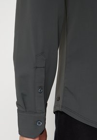 Langarmshirt in donkergrijs, met een gestructureerde stof, manchetten met knopen en een klein logodetail bij de zoom.