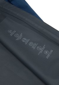 Tela oscura con patrón de cuadricula pequeña que muestra símbolos de cuidado blancos y texto que indica resistencia al agua, transpirabilidad, cortavientos y fibras recicladas.
