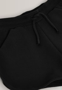 Schwarze Sportshorts aus weichem Stoff. Verfügt über einen elastischen Bund mit gebundenem Kordelzug und Seitentaschen. Glatte Textur, ohne Muster.