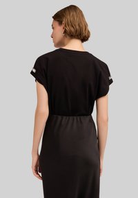 Vestido negro con mangas cortas y cintura ajustada, con una textura suave y sutiles acentos de lentejuelas en el hombro.
