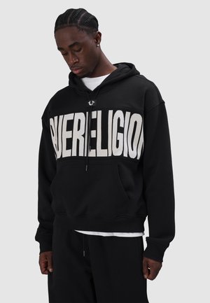 Black hooded sweatshirt featuring large "SUPERRELIGION" text in white, adjustable drawstring, and front pocket. Cotton blend fabric.