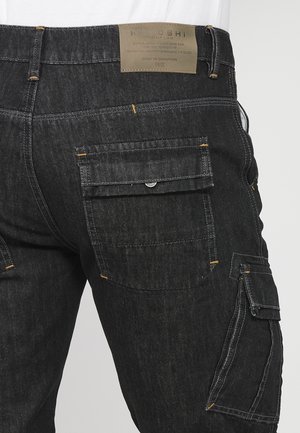 Schwarze Cargo-Jeans mit mehreren Taschen, kontrastierendem gelbem Stich und strukturiertem Finish. Mit einem gebrandeten Lederpatch am Bund.
