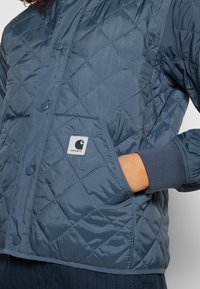 Pikowana, granatowa kurtka puchowa wykonana z nylonu, z zapięciem na guziki, bocznymi kieszeniami i ściągaczami przy mankietach dla zwiększonego komfortu.