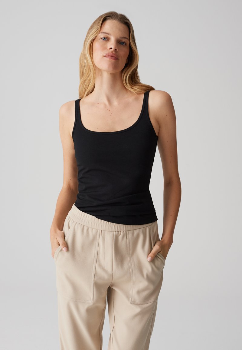 Canotta nera con scollatura a barca, realizzata in tessuto morbido, abbinata a pantaloni beige di taglio loose con tasche laterali e vita elastica.