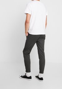 Szare spodnie w cienkie prążki o wąskim kroju, zestawione z białym t-shirtem i czarnymi tenisówkami. Gładka tkanina o swobodnym stylu.