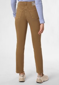 Pantalon slim-fit marron avec une taille mi-haute, poches arrière, et une texture lisse, associé à des chaussures de sport beiges et un haut à côtes bleu clair.