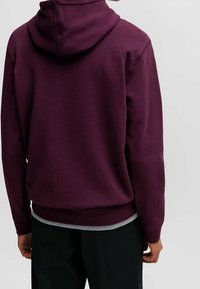 Pullover hoodie i djup lila, tillverkad av mjukt tyg. Har en känguruficka, ribbade ärmslut och en avslappnad passform med huva.