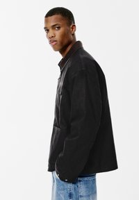 Czarna koszula overshirt w luźnym kroju, z brązowym kołnierzykiem, kieszonką na piersi i zapinanymi mankietami. Miękka tkanina o teksturowanym wykończeniu.