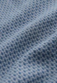 Tissu bleu clair texturé présentant un motif en nid d'abeille, avec une surface lisse et un design tissé. Le matériau semble respirant et flexible.