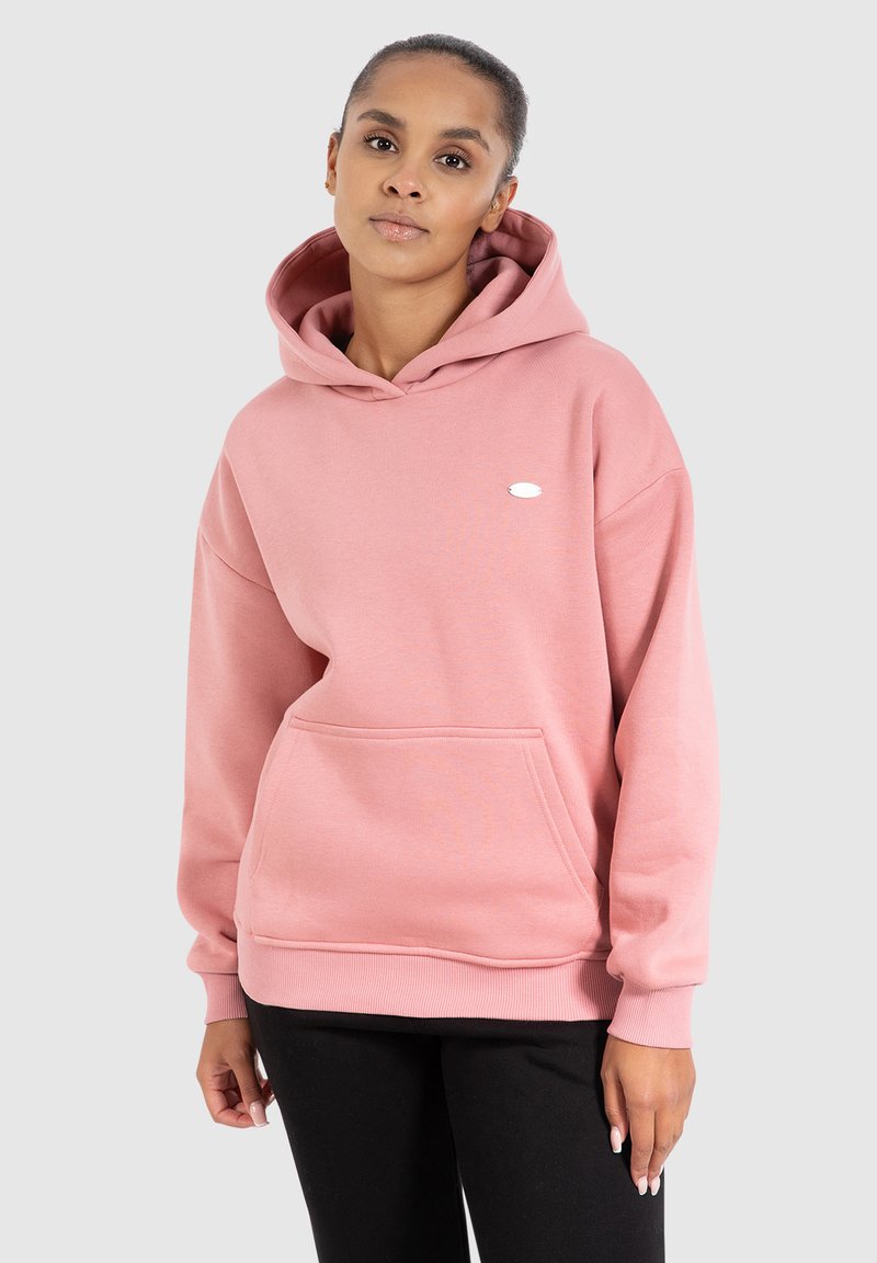 Hoodie rose clair avec une poche avant, capuche à cordon, et un petit logo ovale sur la poitrine. Tissu doux et coupe décontractée.