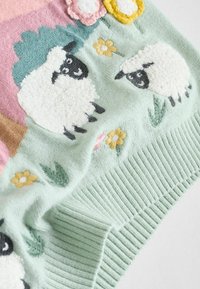 Pled o szydełku w jasnym zielonym kolorze z puszystymi białymi owcami o czarnych pyskach, różowym i żółtym haftem kwiatowym oraz prążkowanym brzegiem.