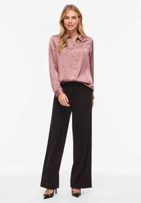 Satīna, mīkstā mauves krāsā ar garām piedurknēm blūze ar pogu aizdari, kombinēta ar augsta vidukļa platām melnām biksēm un atbilstošiem melniem augstpapēžu apaviem ar akcentiem.