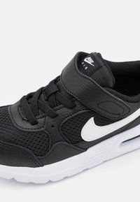 Mustat urheilukengät, joissa on nahka- ja verkkopinta, valkoinen Nike-merkki, tekstuuripinta ja säädettävä hihna nauhojen päällä. Valkoinen pohja.