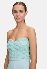 Sukienka bez ramiączek z miętowozielonym kwiatowym korpusem z warstwowym materiałem różanym oraz gładką, lejącą się spódnicą.