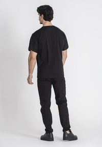 Camiseta de algodón negro con un ajuste relajado, combinada con jeans negros. Diseño simple, textura suave, sin patrones ni logotipos visibles.