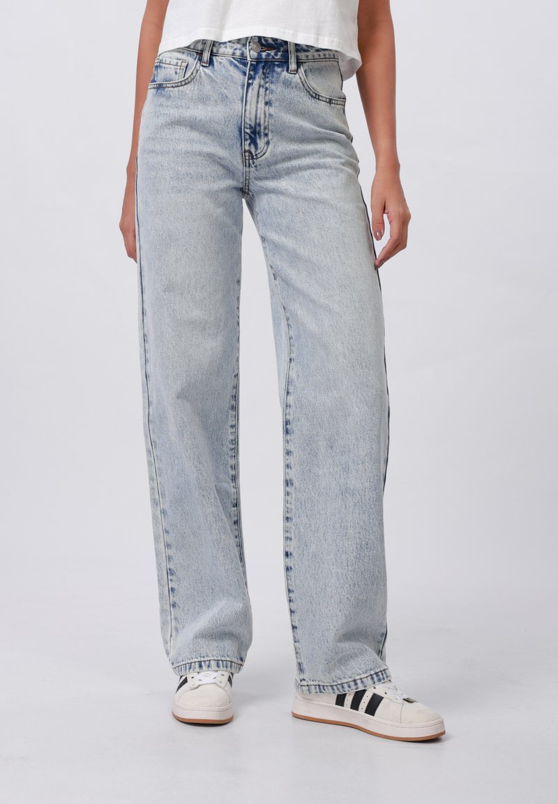 Jeans en denim bleu clair à jambe large et taille haute, dotés d'un design classique à cinq poches et d'un léger délavage sur le tissu. Baskets blanches avec des rayures noires.