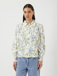 Blommig skjorta med knappar i vitt med blåa och gröna blommor, samlade ärmar och elastiska muddar. Matcher med ljusblå denimjeans.