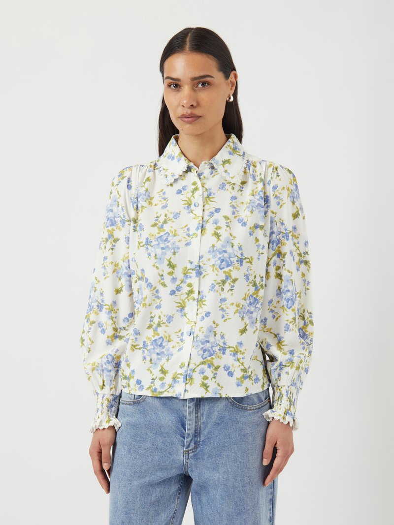 Blommig skjorta med knappar i vitt med blåa och gröna blommor, samlade ärmar och elastiska muddar. Matcher med ljusblå denimjeans.