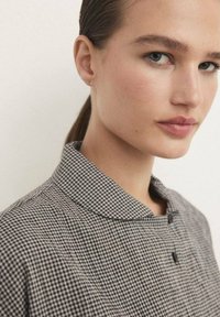 Camicia con colletto in tessuto a scacchi bianco e nero, caratterizzata da bottoni, materiale morbido e design strutturato. Senza decorazioni visibili.