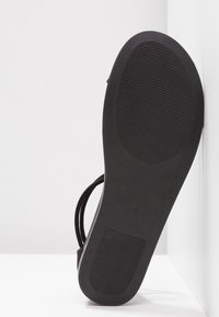 Base de sandale noire avec une semelle en caoutchouc texturé, présentant un design de bride supérieure lisse. La semelle est plate et dispose de rainures horizontales pour une meilleure adhérence.