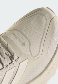 Béžová športová topánka s textúrovaným zvrškom so vzorom mriežky, spevnenou špicou a gumovou podrážkou s detailom "LIGHT BOOST".