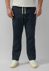 Marineblauwe tapered broek van lichtgewicht stof, met zijzakken en een trekkoord in de taille. Gecombineerd met witte sneakers.