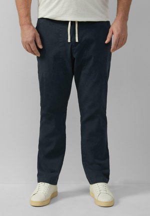 Marineblauwe tapered broek van lichtgewicht stof, met zijzakken en een trekkoord in de taille. Gecombineerd met witte sneakers.