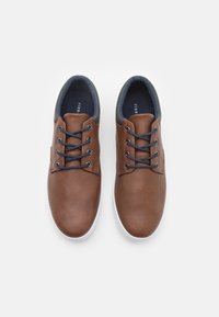 Baskets en cuir marron avec une texture lisse, bout rond et lacets navy. Elles sont dotées d'une semelle en caoutchouc blanc et d'un col rembourré pour plus de confort.