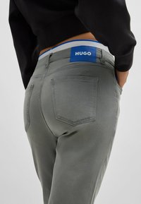 Harmaat farkut sisältävät sinisen HUGO-logopatchin vyötäröllä, tavalliset takataskut ja sileän pinnan.