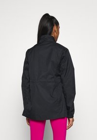 Svart lätt jacka med hög krage och långa ärmar, som har en insvängd midja och en slät, matt yta.