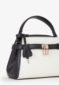 Borsa in bianco e nero con una forma strutturata, realizzata in pelle e tela, con accessori in oro e un piccolo dettaglio a forma di lucchetto.