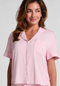 Kortærmet, lichtroze pyjamabroek in zachte stof. Voorzien van een notch-kraag, knoopsluiting en een voorzak. Soepele textuur, ontspannen pasvorm.