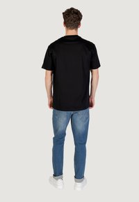 T-shirt nera a maniche corte con taglio dritto, abbinata a jeans blu. La t-shirt ha una finitura liscia e un design minimalista.