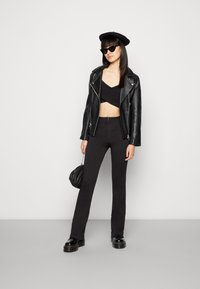 Jaqueta de motociclista de couro preto sobre um top preto curto, combinada com calças pretas ajustadas e botas pretas robustas. Os acessórios incluem uma boina preta e óculos de sol.