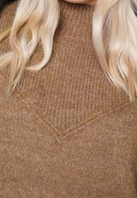 Pull en tricot marron à col montant, avec un motif texturé et un design en forme de V à l'avant. Tissu doux et chaud.