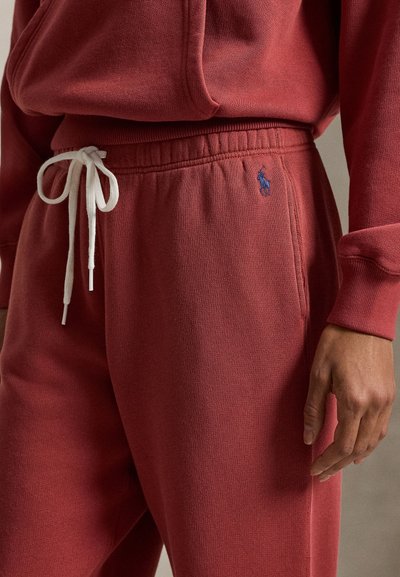 Rød genser med teksturert overflate og ribbestrikkede mansjetter, med hvit snor og en liten blå brodert logo ved hoften.