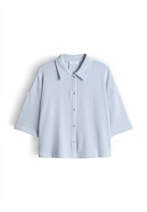 Chemise à manches courtes bleu clair avec col large et coupe ample, présentée sur un fond blanc.