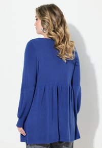 Blå ribbad tröja med lång ärm och plisserad baktill. Mjuk textur, avslappnad passform, avslutad med en rund nederkant.