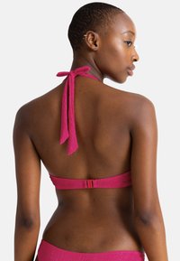 Rožinė halter stiliaus bikini viršutinė dalis su sujungimo juostele, pasižyminti tekstūruota medžiaga ir užsegimu gale.