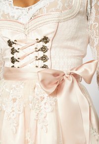 Robe rose avec une superposition en dentelle, un devant style corset avec un laçage décoratif, et une ceinture en satin ornée de détails brodés de fleurs.