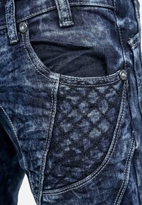 Jeans in denim con una finitura blu scuro sbiadita, caratterizzati da dettagli trapuntati nelle tasche e hardware argentato sul davanti.