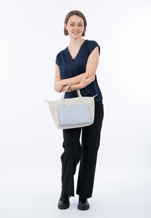 Lichtgrijze totebag met een blauwe voorkant, met dubbele handvatten en een gestructureerde vorm. Draagt door een persoon in een marineblauw top en zwarte broek.