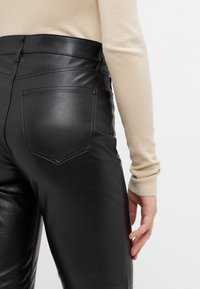 Svarta läderbyxor med hög midja, med två bakfickor och synliga sömmar. Mjuk textur och en figurnära design.